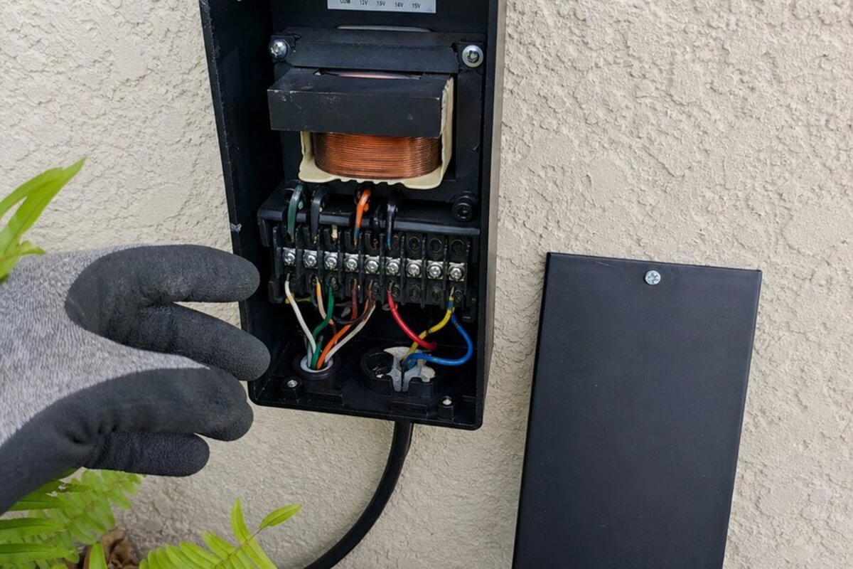 Open low-voltage landscape lighting transformer on a Palm Bay stucco wall with terminals visible during a repair check